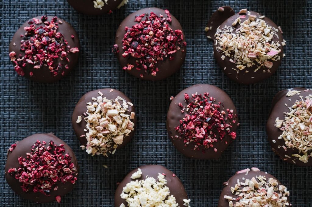 Menu Assorted chocolate bites topped with dried berries on a textured surface.