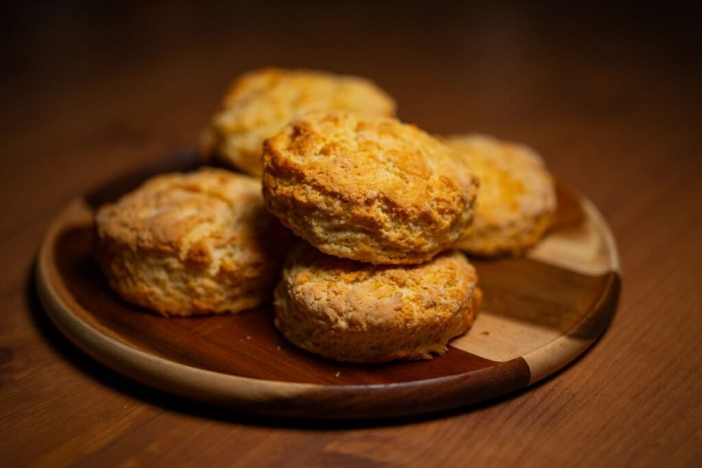 Menu Freshly baked golden biscuits stacked on a wooden plate, perfect for breakfast or tea time.