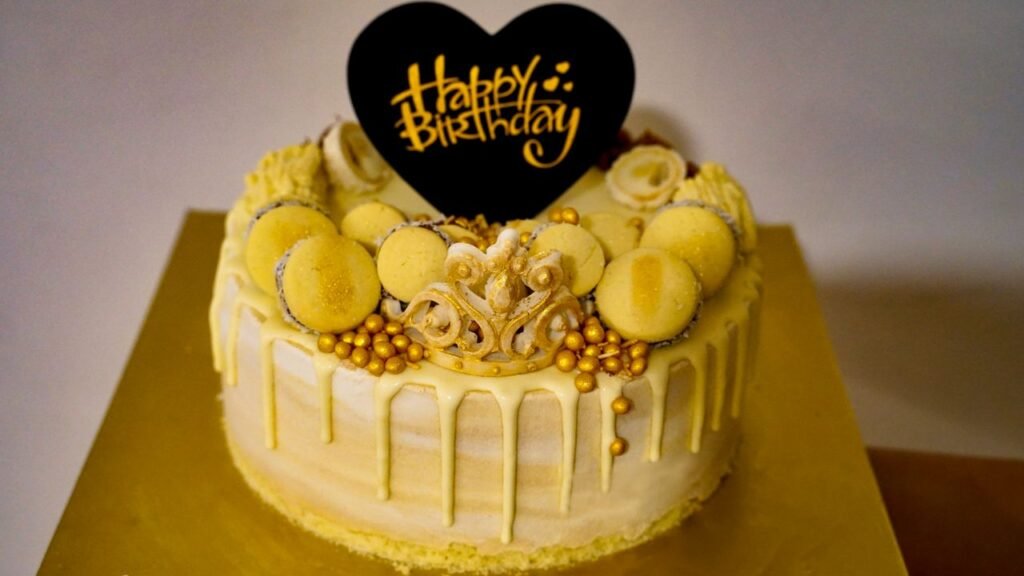 Menu Stylish yellow birthday cake adorned with macarons and golden accents, perfect for celebrations.